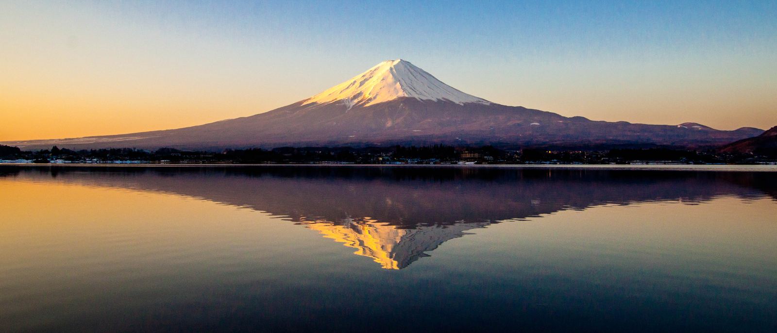 A mountain at first light, reflected in still water. The mountain is the practice itself; the reflection is what an AI assistant tells a customer about it.